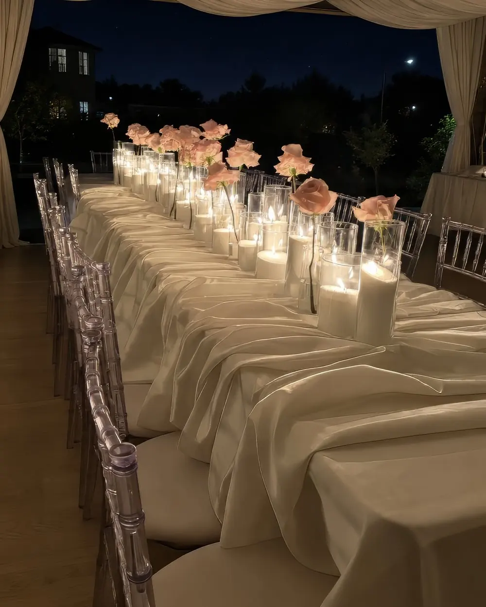 A styled long table under a marquee at night, lit with candles and roses